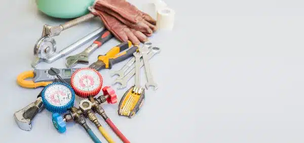 Various tools including wrenches, pliers, a folding utility knife, pressure gauge, and gloves are arranged on a light surface.