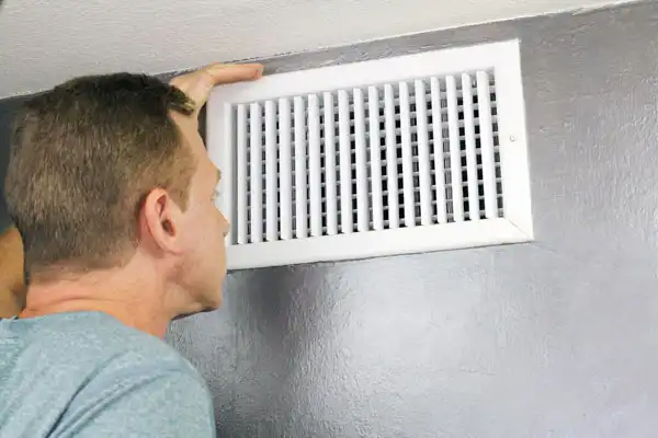 A person inspects an air vent on a gray wall.