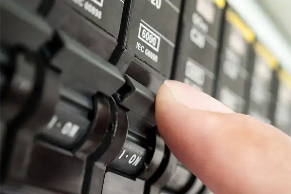 A person flipping a switch on an electrical circuit breaker panel, with the panel labeled "IEC 60898" and switches marked "ON" and "OFF.