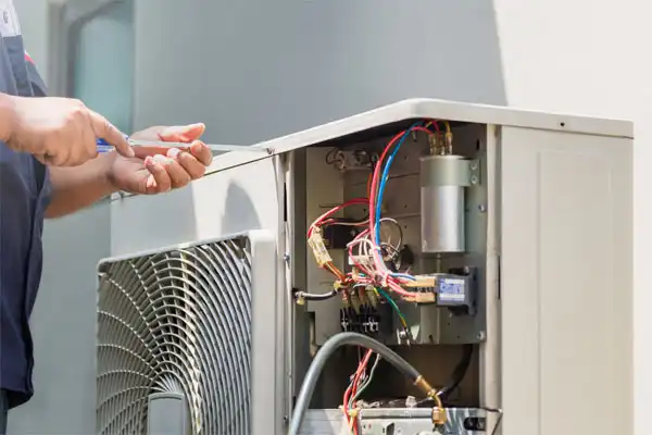 Technician using a screwdriver to repair an outdoor air conditioning unit with exposed wiring and components.