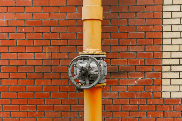 Orange pipe with a large valve mounted on a red brick wall, transitioning to a beige brick section on the right.
