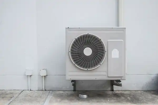 Outdoor air conditioning unit mounted on a wall with visible pipes and wiring.