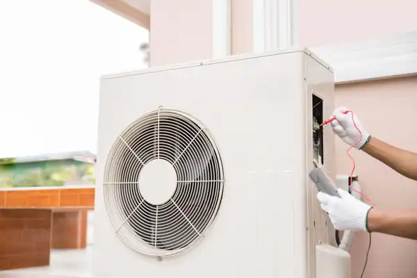 Person in gloves repairing an outdoor air conditioning unit with tools.