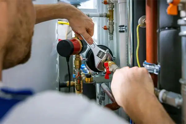 A person uses a wrench to adjust plumbing pipes and valves in a mechanical room.