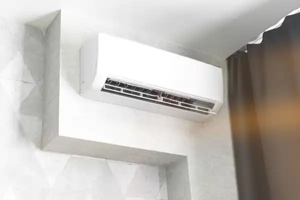 White wall-mounted air conditioning unit installed in the corner of a room, with a dark curtain partially visible to the right.