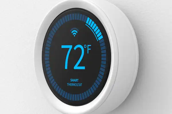 A smart thermostat mounted on a wall displays a temperature of 72°F, with a blue digital interface and Wi-Fi symbol.