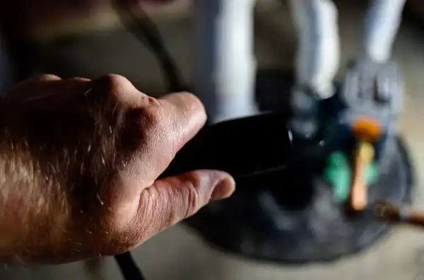 Close-up of a person's hand holding a cable or hose, with blurred industrial equipment visible in the background.
