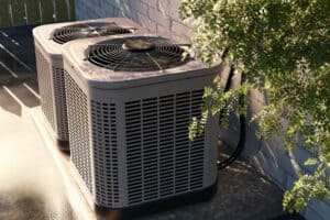 Two outdoor air conditioning units sit on a concrete platform next to a brick wall, partially shaded by tree branches—a testament to quality HVAC Services Norwalk CT & White Plains NY residents rely on.